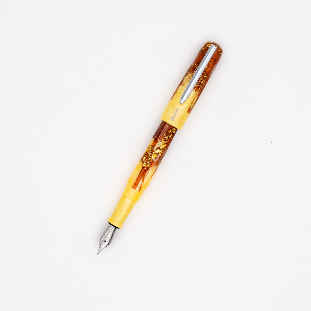 A yellow and amber marbled fountain pen with a yellow band with a silver nib and clip. The BENU logo is engraved with silver under the clip. The cap is posted on the pen and it is photographed diagonally on a clean white background.