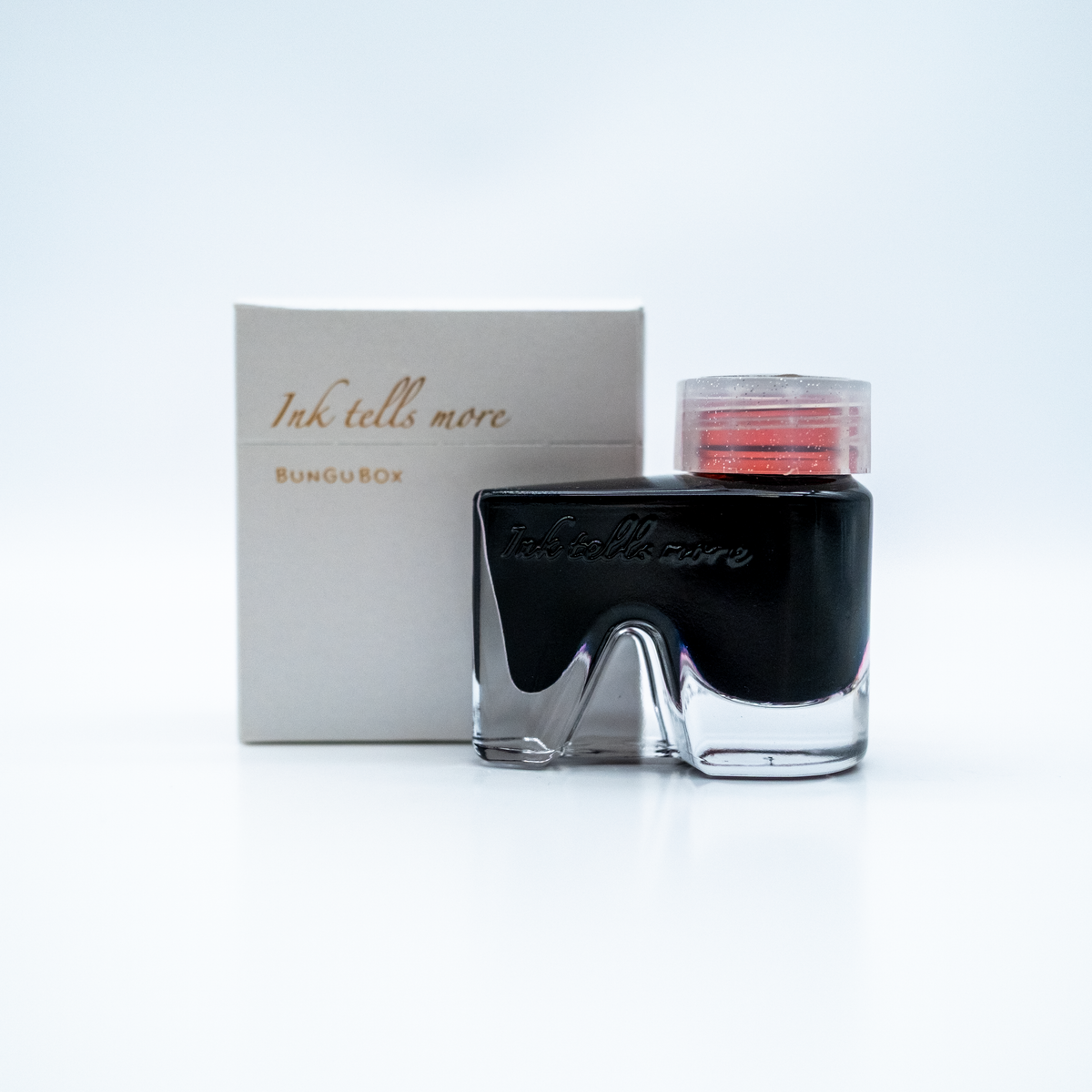A bottle of Ink Tells More from BunguBox with a clear cap showing the red threading inside, displayed in front of its packaging box on a white background.
