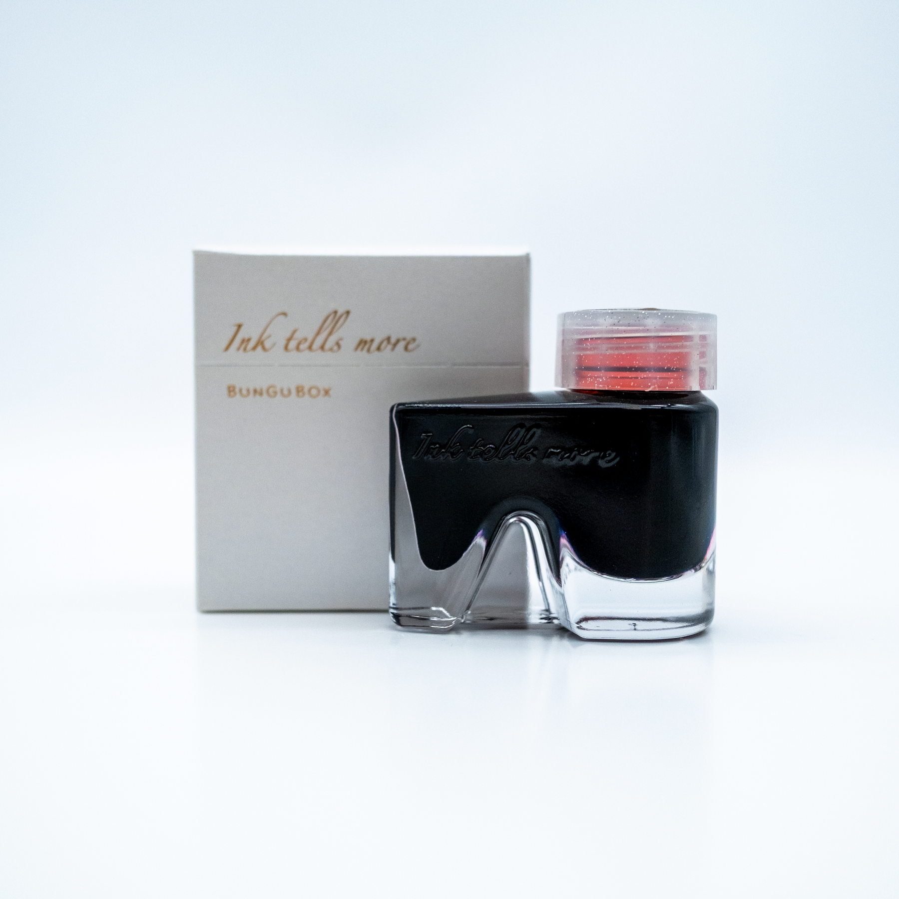 A bottle of Ink Tells More from BunguBox with a clear cap showing the red threading inside, displayed in front of its packaging box on a white background.