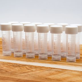 Twelve 5ml clear plastic sample vials with white ribbed caps, arranged on a wooden surface against a light background.
