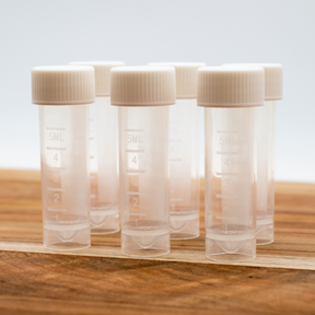 Six 5ml clear plastic sample vials with white ribbed caps, arranged on a wooden surface against a light background.