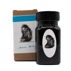 A bottle of fountain pen ink with a white oval label featuring a black and white portrait, standing next to its brown cardboard box with a blue band and a printed portrait on a white background.