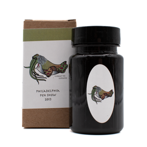 A bottle of Organics Studio 'Join or Die' in front of its brown box with a white and olive green label and black text on a white background.